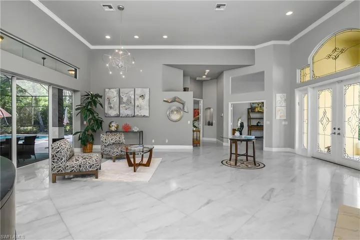 Formal Living area featuring a high ceiling, french doors, crown molding, suspended lighting, and light marble finish floors