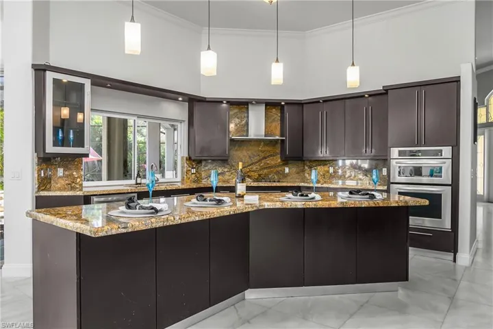 Kitchen with backsplash, light stone countertops, stainless steel double oven, decorative light fixtures, and ornamental molding