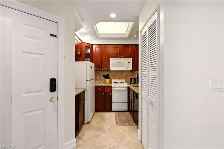 Kitchen with white appliances, backsplash, light tile patterned flooring, light stone counters, and recessed lighting