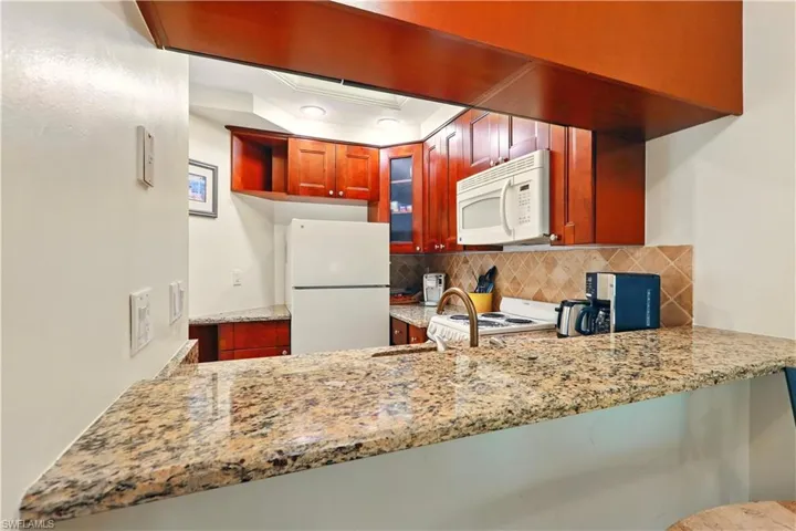 Kitchen with white appliances, tasteful backsplash, granite counters, and glass insert cabinets