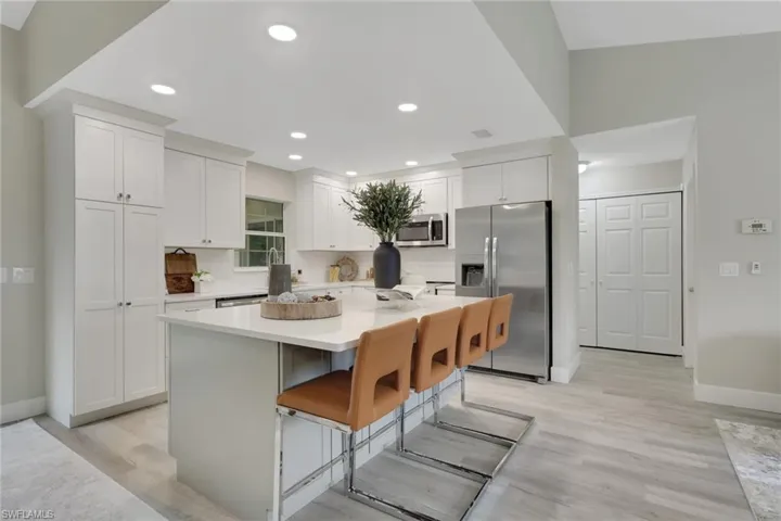 Bright kitchen featuring white shaker cabinetry, stainless steel appliances, a center island with countertop seating, recessed lighting, and wood-finish flooring