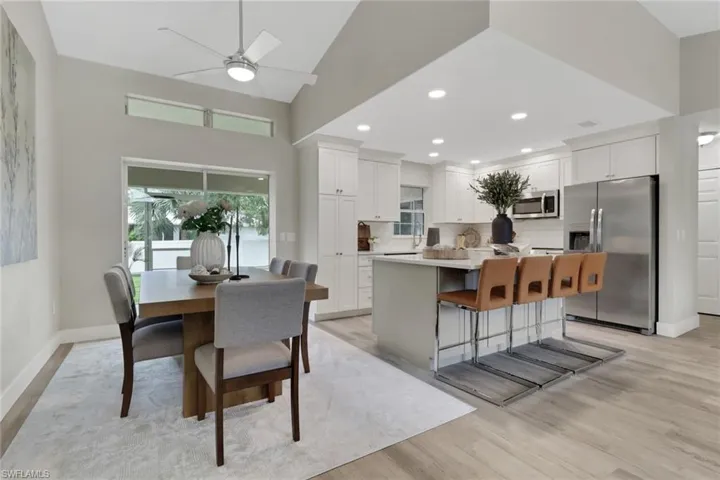 Open-concept living space featuring a vaulted ceiling with a contemporary ceiling fan, wood-finish flooring, and a dining area with a large window