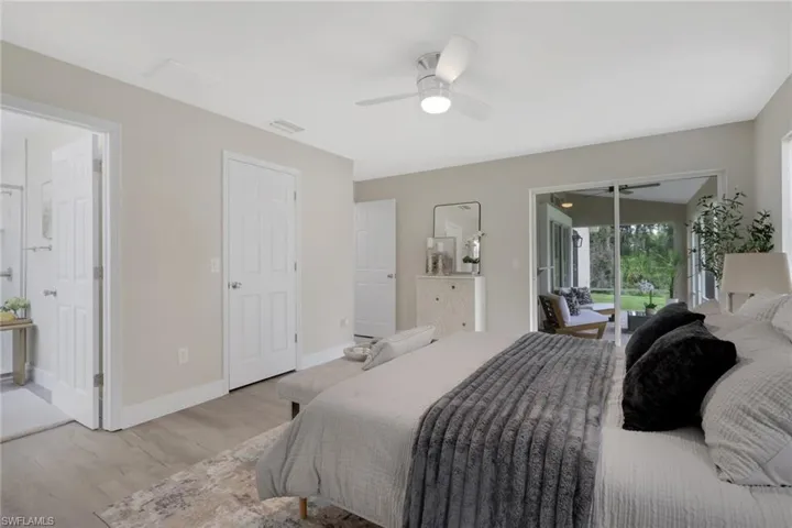 Spacious bedroom featuring light wood-finish flooring, a ceiling fan with integrated lighting, and a sliding glass door opening to a screened outdoor living area