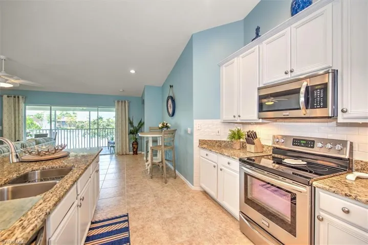 Kitchen with ceiling fan, white cabinets, stainless steel appliances, and vaulted ceiling