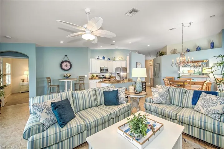 Living room featuring vaulted ceiling, ceiling fan with notable chandelier, and light tile patterned floors