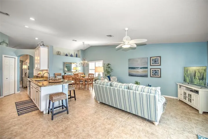 Living room featuring light tile patterned flooring, ceiling fan with notable chandelier, sink, and lofted ceiling