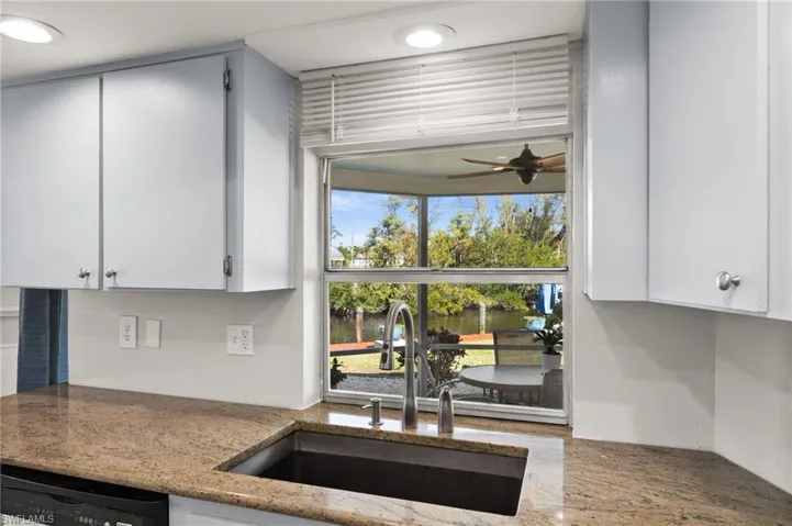 Kitchen with light stone counters, dishwashing machine, ceiling fan, sink, and white cabinetry