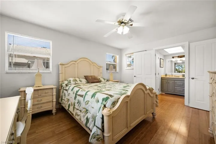 Bedroom with ceiling fan, dark wood-type flooring, connected bathroom, and multiple windows
