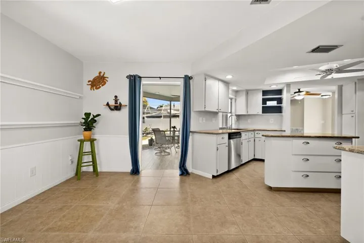 Kitchen with dishwasher, sink, ceiling fan, light tile patterned floors, and white cabinetry