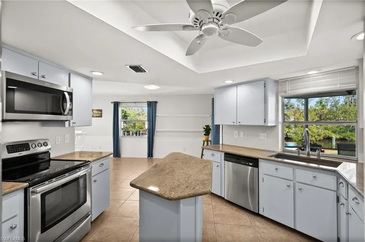 Kitchen with ceiling fan, sink, light tile patterned floors, a kitchen island, and appliances with stainless steel finishes