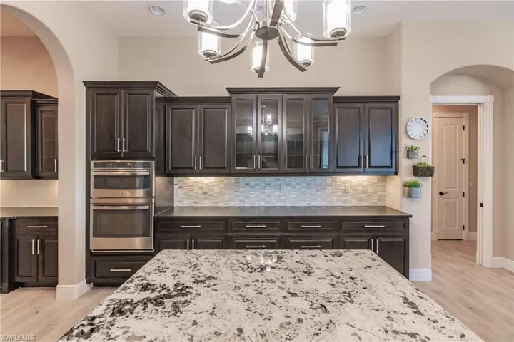 Kitchen with light hardwood / wood-style flooring, a notable chandelier, double oven, decorative light fixtures, and decorative backsplash