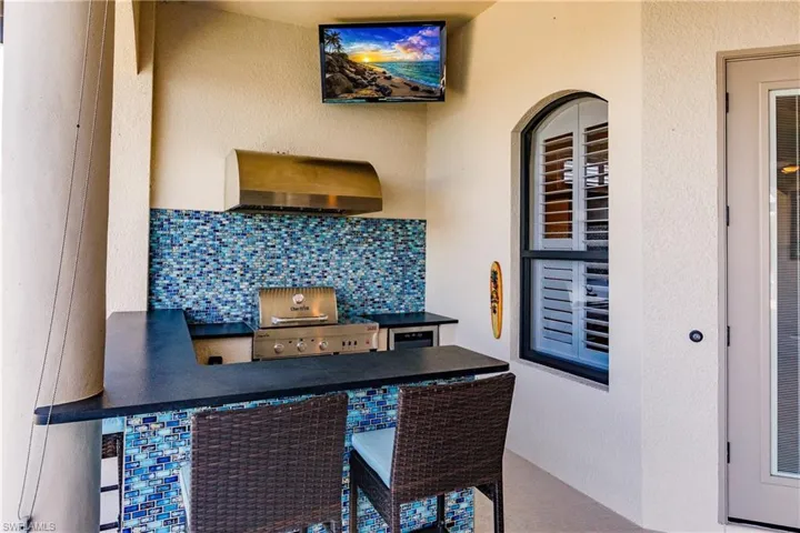 Outdoor Kitchen featuring bar top, TV mounted on wall, grill with exhaust hood and decorative backsplash