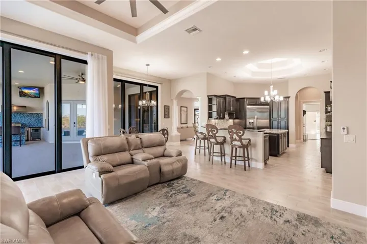 Living room with french doors, light wood-type flooring, a tray ceiling, and an inviting chandelier