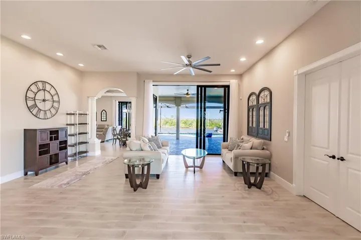Living room with 9 ft sliding impact doors, french doors to owners suite, light hardwood / wood-style floors, ceiling fan, and decorative columns
