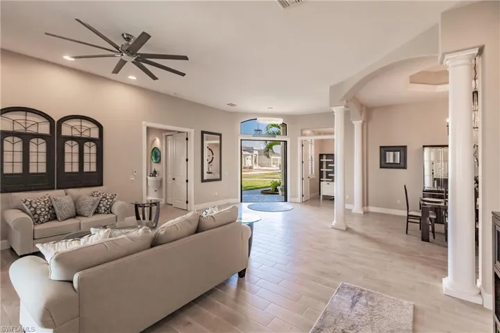 Front Doors open in living room featuring ceiling fan and formal dining with chandelier, decorative columns, and light hardwood / wood-style floors