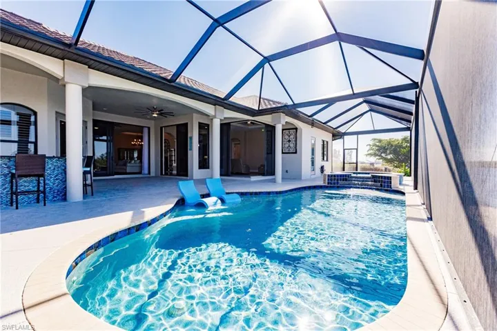 View of pool featuring exterior bar, ceiling fan, glass enclosure, a patio area, and  hot tub