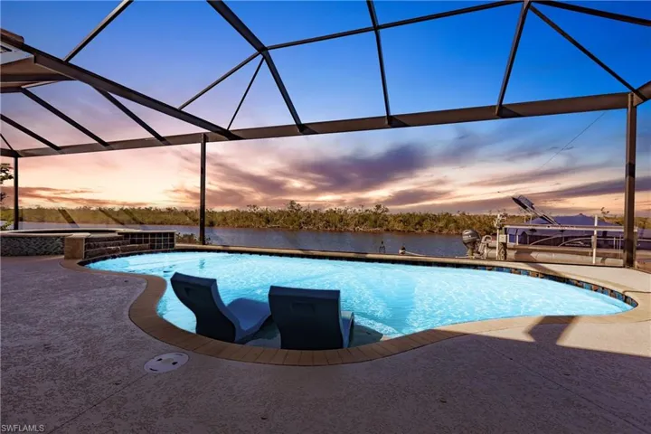 Pool at dusk featuring a patio area and a lanai with super screen. Boat Dock with Lift in background.