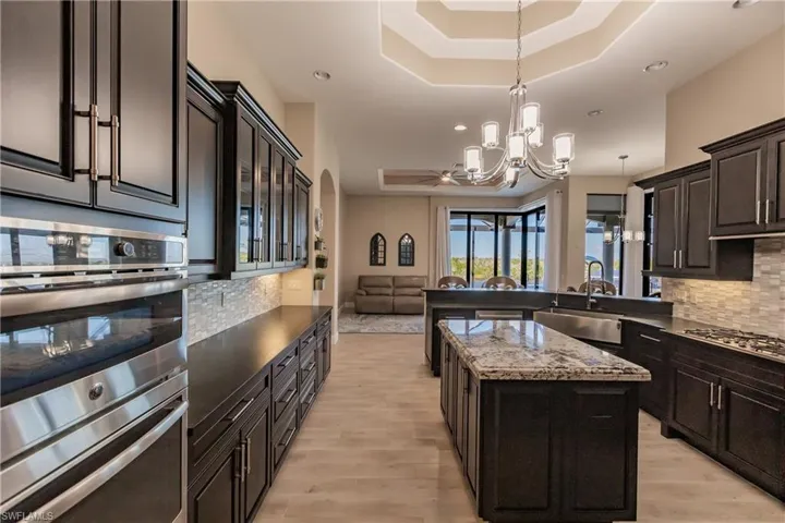 Kitchen featuring decorative backsplash, stainless steel appliances, a raised ceiling, an inviting chandelier, and a kitchen island