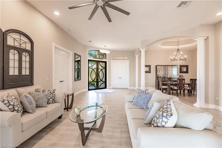 Living room featuring ceiling fan and formal dining with chandelier, decorative columns, and light hardwood / wood-style floors