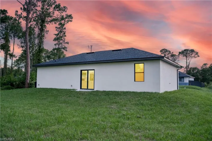 Back of house with stucco siding, a yard, and a shingled roof