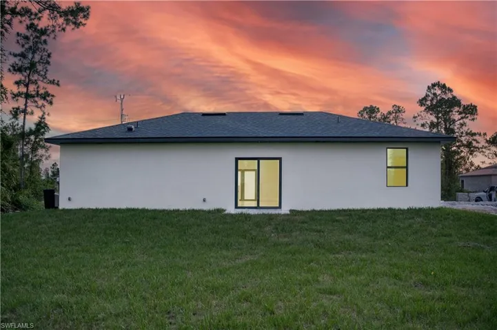 Back of house at dusk with stucco siding, a lawn, and roof with shingles