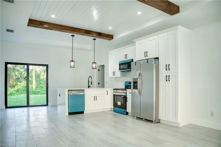 Kitchen with stainless steel appliances, a peninsula, tasteful backsplash, white cabinets, and a wood ceiling with exposed beams