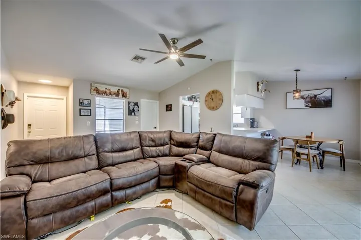 Living room featuring lofted ceiling, ceiling fan, and light tile patterned flooring