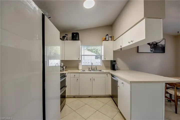 Kitchen featuring light tile patterned floors, appliances with stainless steel finishes, kitchen peninsula, sink, and white cabinetry