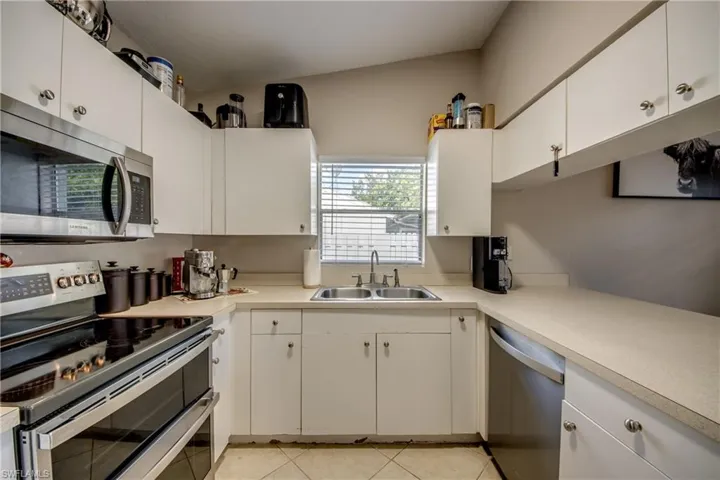 Kitchen with white cabinets, appliances with stainless steel finishes, light tile patterned floors, and sink