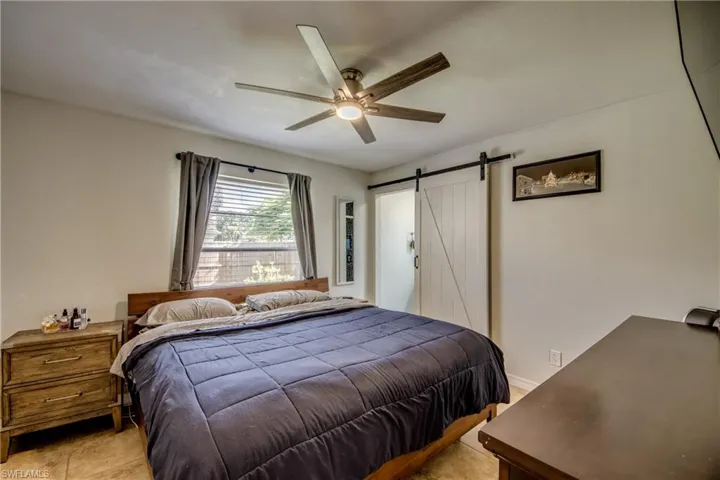 Bedroom with a barn door, ceiling fan, and light tile patterned floors
