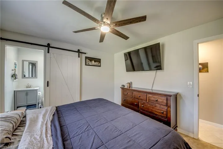 Bedroom featuring ceiling fan, light tile patterned floors, ensuite bathroom, and a barn door