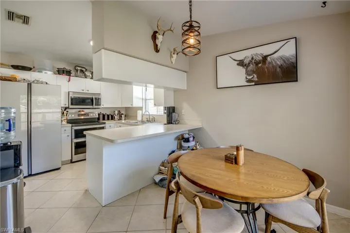Kitchen with white cabinets, stainless steel appliances, sink, kitchen peninsula, and light tile patterned flooring