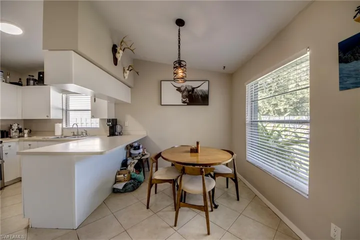 Kitchen with white cabinetry, light tile patterned floors, decorative light fixtures, kitchen peninsula, and sink