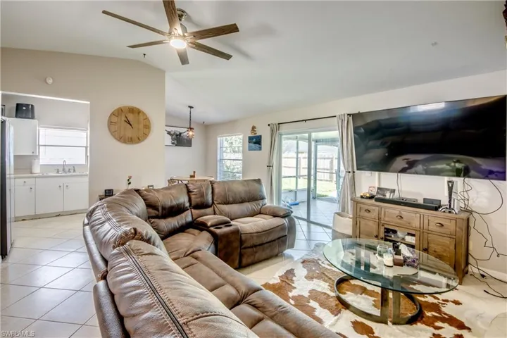 Living room with vaulted ceiling, light tile patterned floors, sink, and ceiling fan