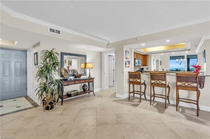 Kitchen with an inviting chandelier, a tray ceiling, light tile patterned flooring, kitchen peninsula, and a breakfast bar area / virtually enhanced image