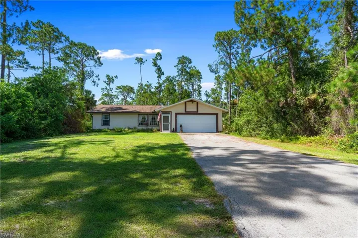 View of front facade featuring driveway, a front yard, stucco siding, and a garage