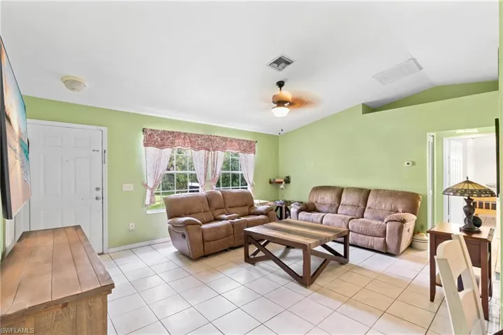 Living room with light tile patterned floors, a ceiling fan, and vaulted ceiling