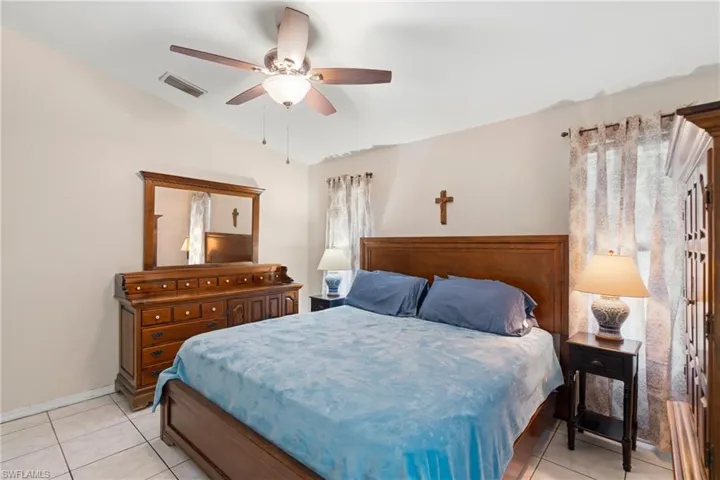 Bedroom with vaulted ceiling, light tile patterned floors, and a ceiling fan