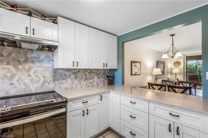 Kitchen with electric range, white cabinetry, decorative backsplash, under cabinet range hood