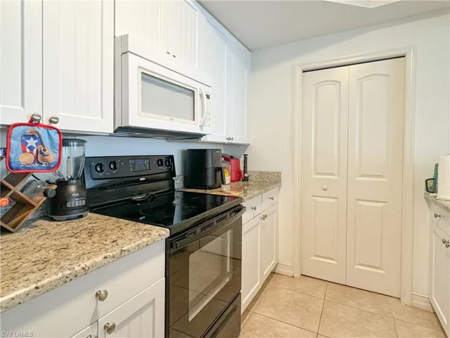 Kitchen with white cabinetry, black electric range, light tile patterned floors, and light stone countertops