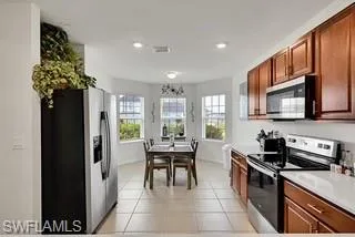 Kitchen featuring stainless steel appliances, light tile patterned floors, light countertops, and brown cabinetry