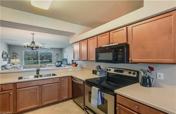 Kitchen featuring stainless steel appliances, pendant lighting, light countertops, a chandelier, and brown cabinetry