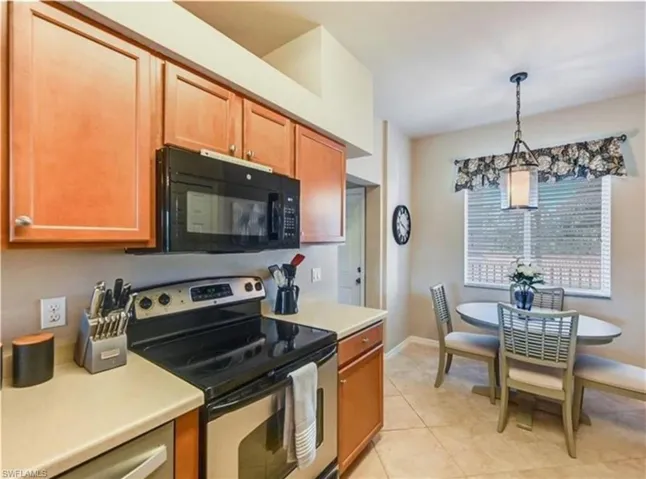 Kitchen featuring stainless steel range with electric stovetop, light countertops, black microwave, and hanging light fixtures