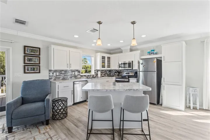 Kitchen with appliances with stainless steel finishes, white cabinetry, a kitchen breakfast bar, decorative light fixtures, and crown molding