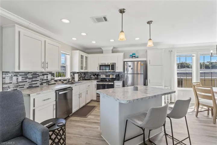 Kitchen with a breakfast bar, backsplash, white cabinets, stainless steel appliances, and ornamental molding