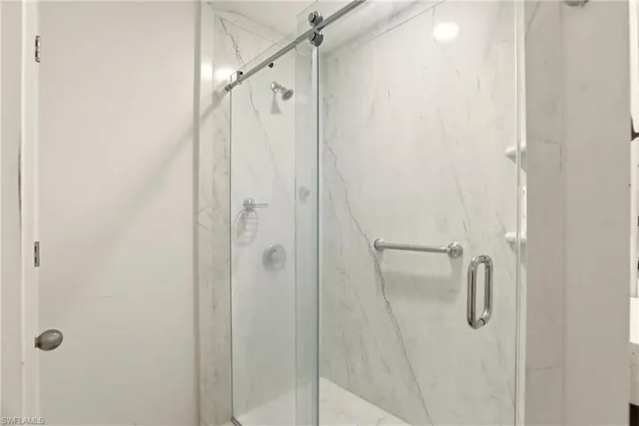 Glass-enclosed shower with a sliding door, marble-patterned wall panels, a built-in shower niche, and polished chrome fixtures