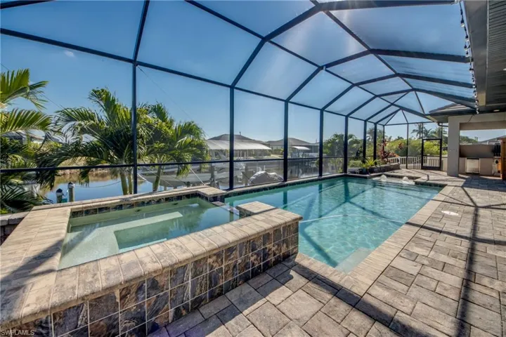 View of swimming pool featuring a sunroom, a pool with connected hot tub, a patio, glass enclosure, and a water view