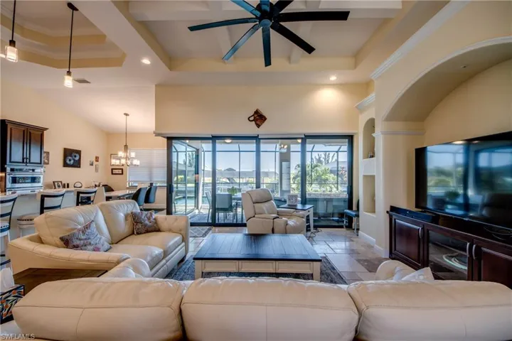 Living area with stone tile flooring, healthy amount of natural light, a ceiling fan, a chandelier, and a high ceiling
