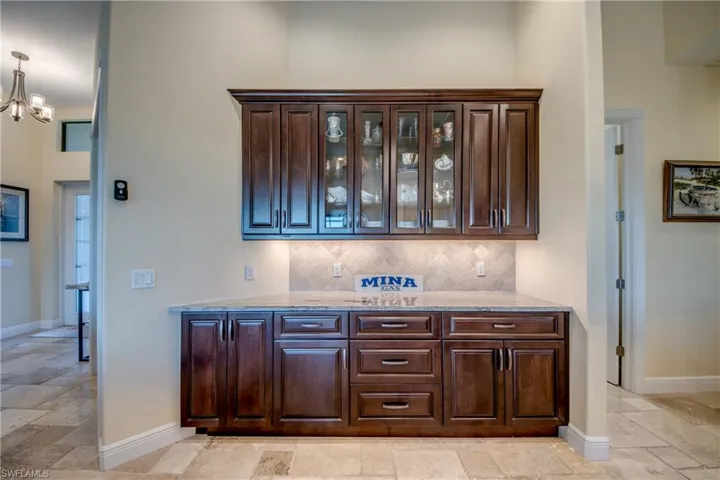 Bar with light stone countertops, glass insert cabinets, dark brown cabinetry, and stone tile flooring