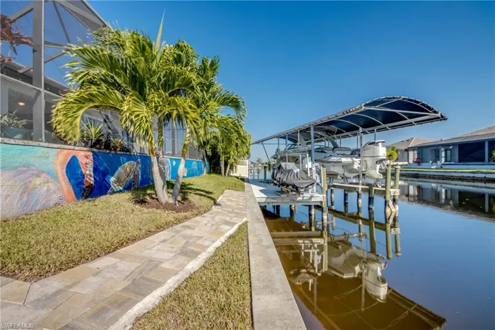 Dock area with glass enclosure, boat lift, a water view, a lawn, and a sunroom